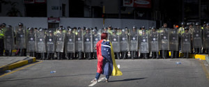 A demonstrator wearing a Venezuelan flag stands in front of police dressed in riot gear during a protest in Caracas, Venezuela, on Saturday, Jan. 24, 2015. Photographer: Wilfredo Riera/Bloomberg via Getty Images